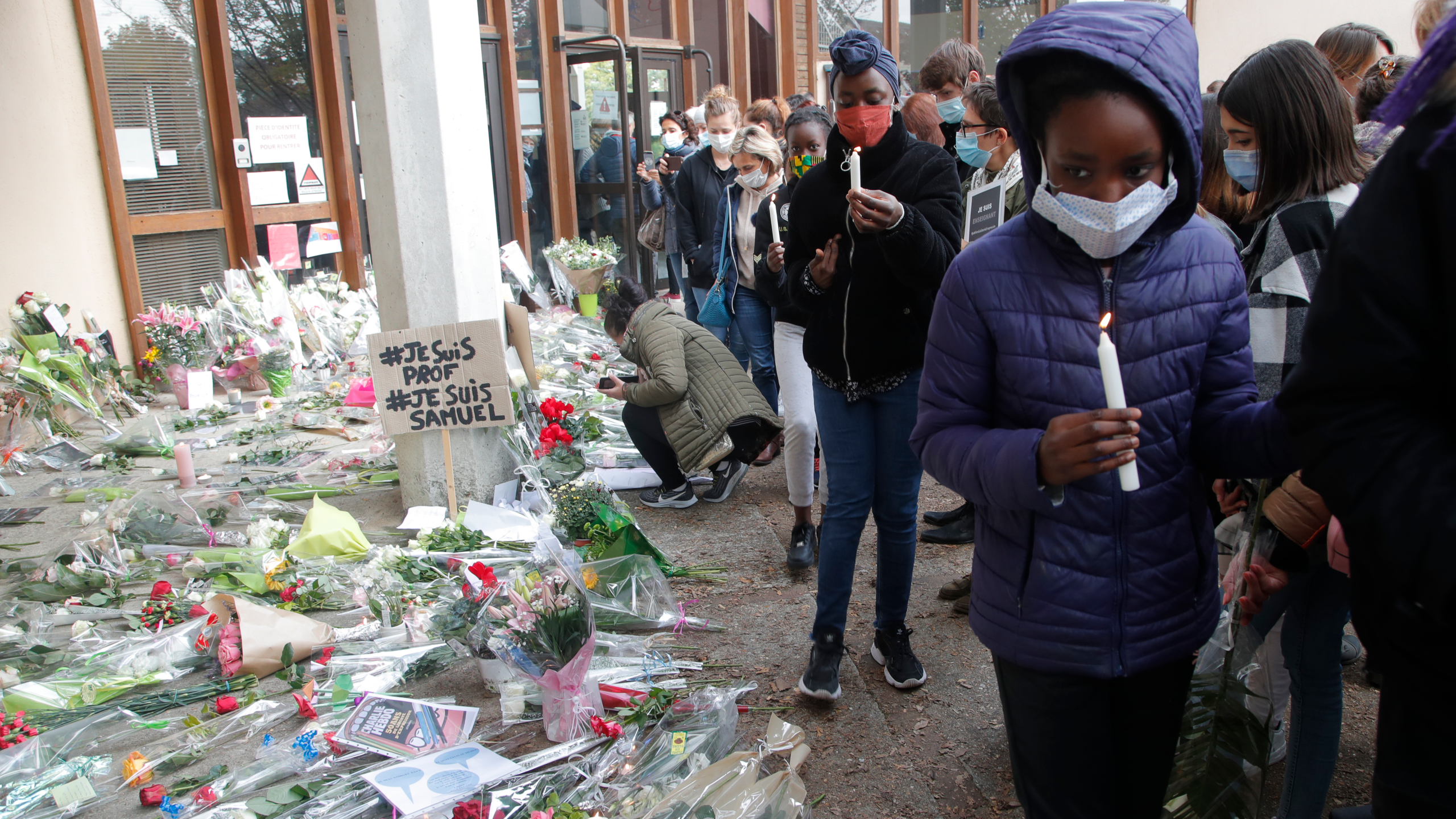 Signs reading 'I am a teacher' and 'I am Samuel' were among flowers laid down as tributes for the teacher.