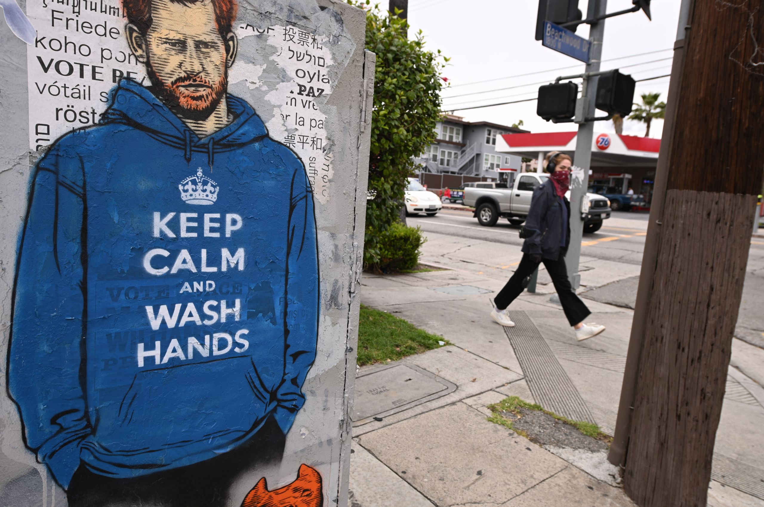 People walk past graffiti of Prince Harry wearing a hoodie reading "Keep Calm and Wash Your Hands," on April 7, 2020, during the coronavirus pandemic in Los Angeles, California.